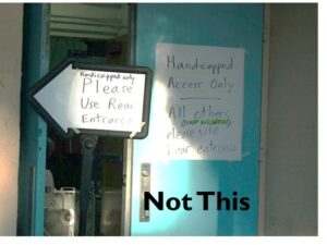 Image of a door to a building with a sign on the door and a sign standing pointing to the left. On the bottom of the image is "Not This." The sign on the door reads "Handicapped Access Only. All others (staff included) please use rear entrance." The sign pointing to the left reads "Handicapped only. Please use rear entrance."