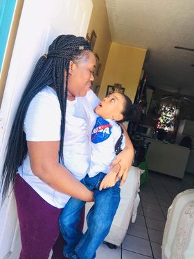 Manoushka, a woman with long box braids half pulled back, holds her son, Devon, a young boy wearing a NASA shirt