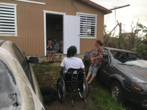 Image of Germán sitting in his wheelchair talking with 2 disabled Hurricane Maria survivors and their mother outside their home.