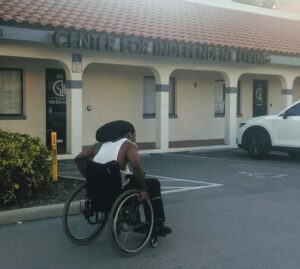 Image of Black disabled man pushing his wheelchair in front of a building with the words Center for Independent Living on it