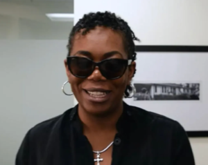Photo of Justice Shorter, a smiling Black woman with her dark hair in two-strand twists, wearing a black shirt and sunglasses.