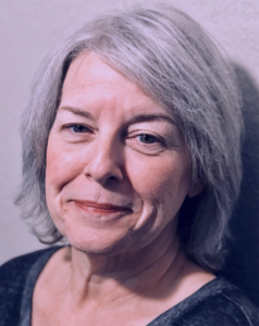 Photo of Shari, an older white woman with grey hair, smiling.