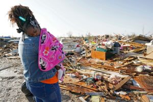 Image of a mother holding her sleeping daughter as she looks out at the vast area of debris where homes used to be. Image by AP Photo/Rogelio V. Solis.