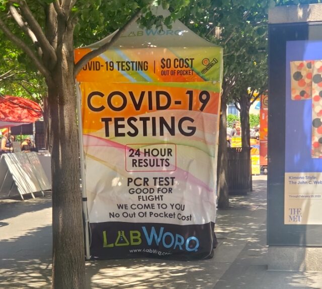A colorful pop-up canopy on a sidewalk promoting free COVID-19 PCR testing.