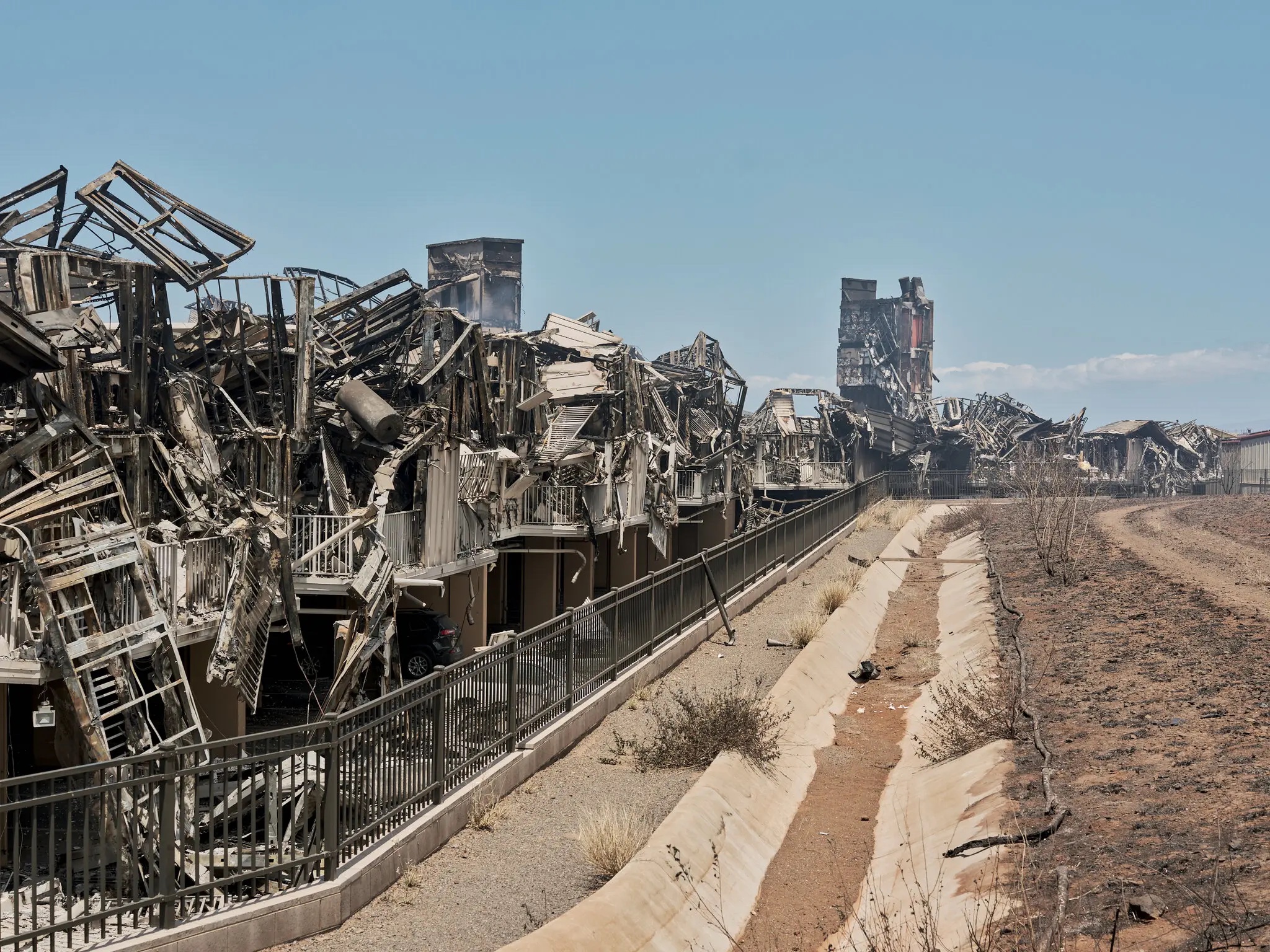 From the town of Lāhainā on the Hawaiian island of Maui, a view of a long row of destroyed buildings, twisted and blackened by fire.