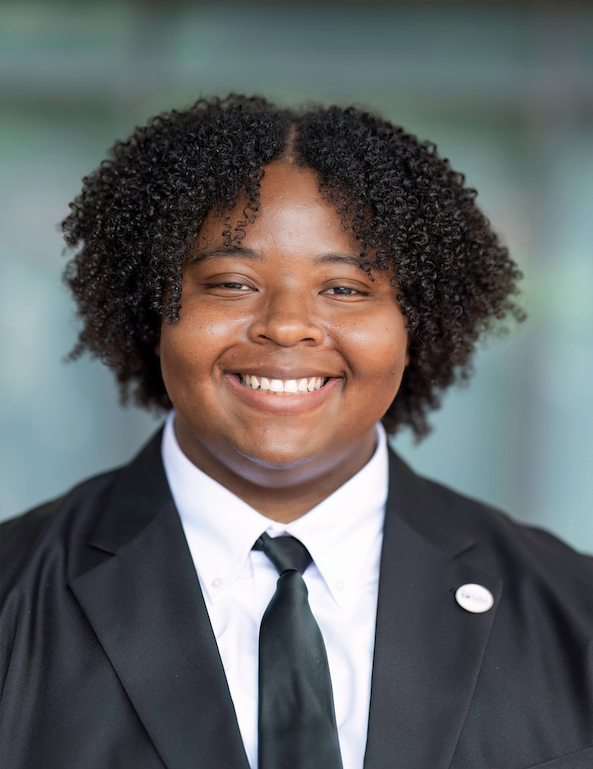 Kevin Moore, a young Black man with medium-length curly hair in a black suit, smiles at the camera.
